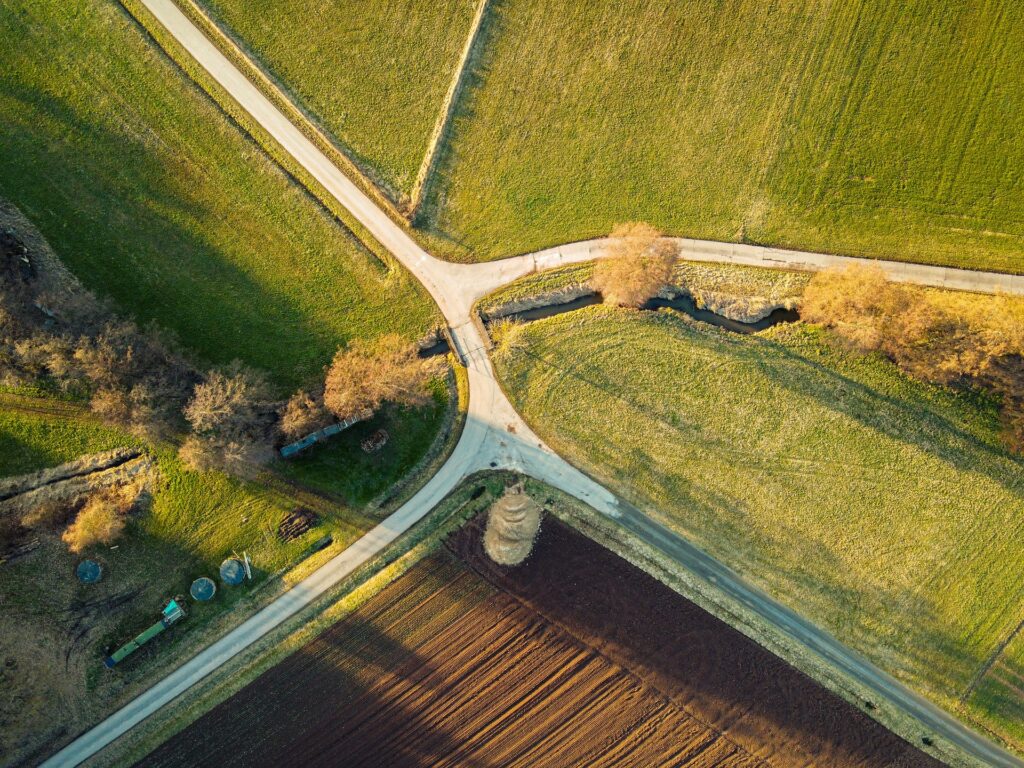 Luftaufnahme von sich kreuzenden Straßen, Feldern, Bäumen und einem kleinen Bach in einer ländlichen Landschaft.