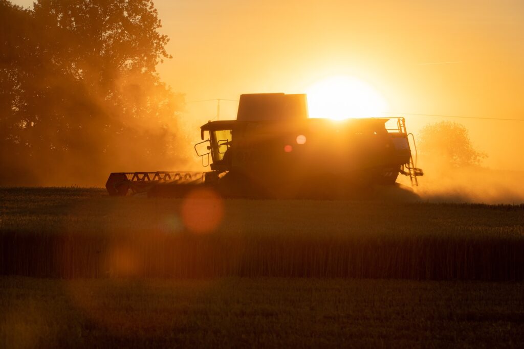 Ein Mähdrescher arbeitet bei Sonnenuntergang auf einem Feld, dessen Silhouette sich vom leuchtend orangen Himmel abhebt.