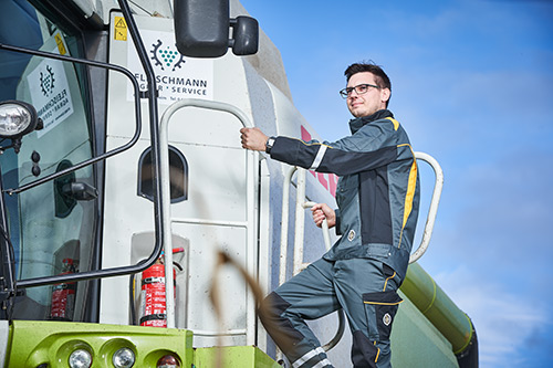 Ein Mann im Arbeitsoverall klettert unter blauem Himmel auf eine grüne Landmaschine.