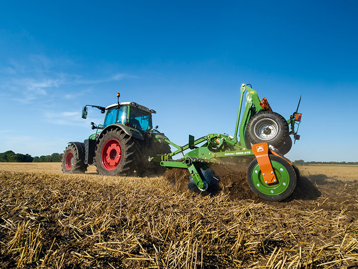 Ein Traktor pflügt ein trockenes, abgeerntetes Feld unter einem klaren blauen Himmel.