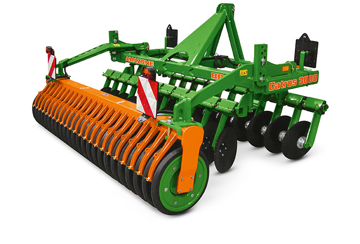 Grün-orangefarbene landwirtschaftliche Scheibenegge mit mehreren Walzen und Messern, mit der Bezeichnung Catros 3000.