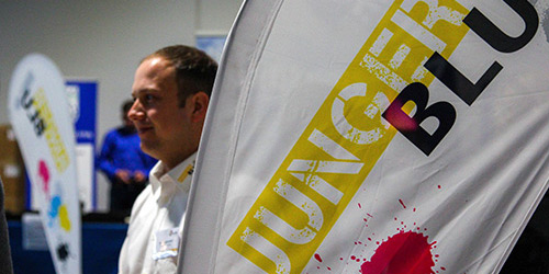 Ein Mann steht neben einer weißen Flagge mit der Aufschrift JUNGER BLUT und bunten Farbspritzern.