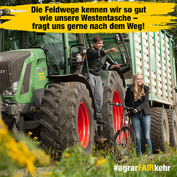Ein Mann auf einem Traktor zeigt auf etwas, während eine Frau mit einem Fahrrad neben ihm steht, beide lächeln in einer ländlichen Umgebung.