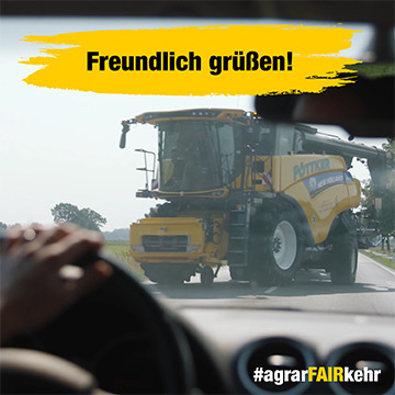 Blick aus einem Auto, das einen großen gelben Mähdrescher auf der Straße zeigt, mit dem Text Freundlich grüßen! darüber.