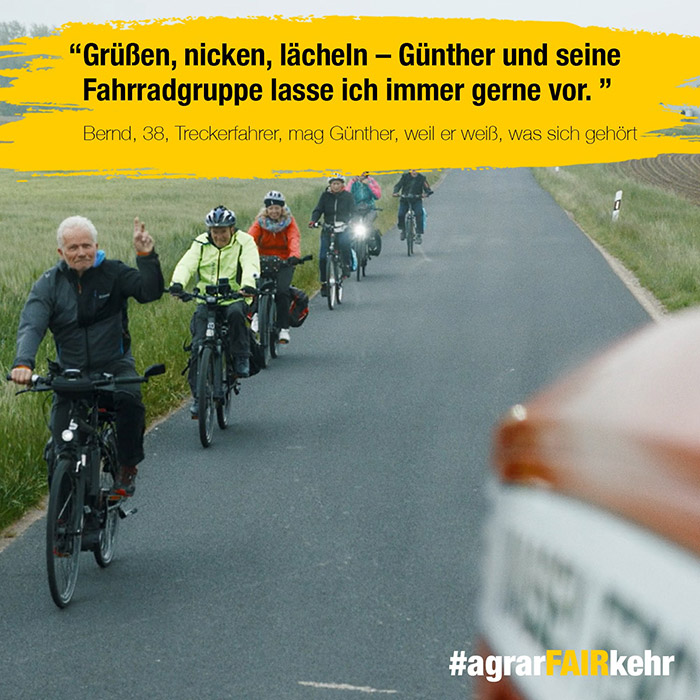 Eine Gruppe von Radfahrern fährt auf einer Landstraße, angeführt von einem älteren Mann, mit Feldern auf beiden Seiten.