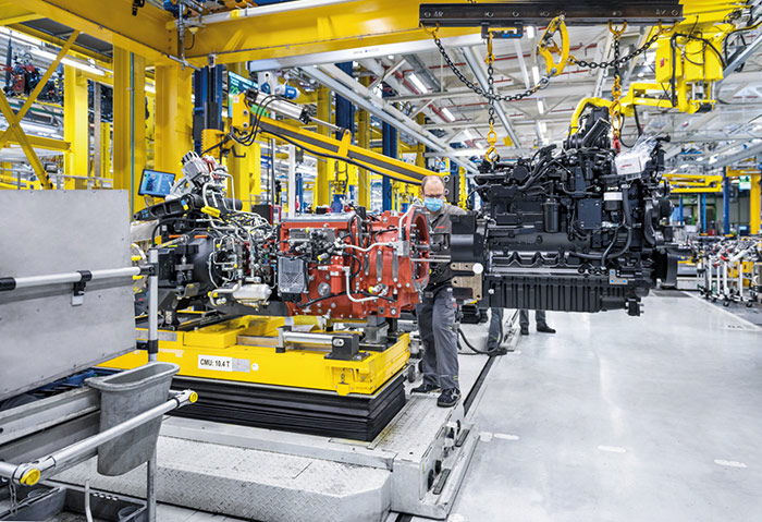 Ein Arbeiter montiert große Maschinenteile in einer hell erleuchteten, modernen Fabrik mit gelben Geräten.