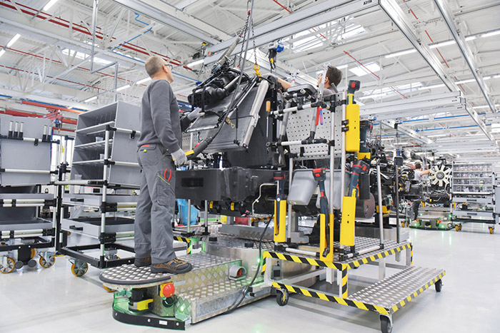 Zwei Arbeiter montieren Maschinenteile an einer Fertigungsstraße in einer Automobilfabrik, umgeben von Werkzeugen und Geräten.