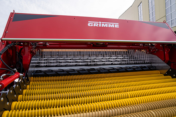 Nahaufnahme einer roten Grimme Landmaschine mit gelben Walzen und Metallstäben, die wahrscheinlich für die Ernte verwendet wurde.