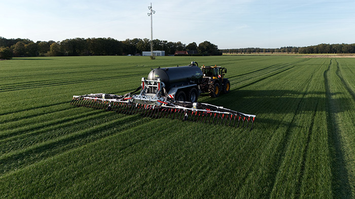 Ein Traktor bringt an einem klaren Tag mit einem breiten Anbaugerät Dünger auf ein großes grünes Feld aus.