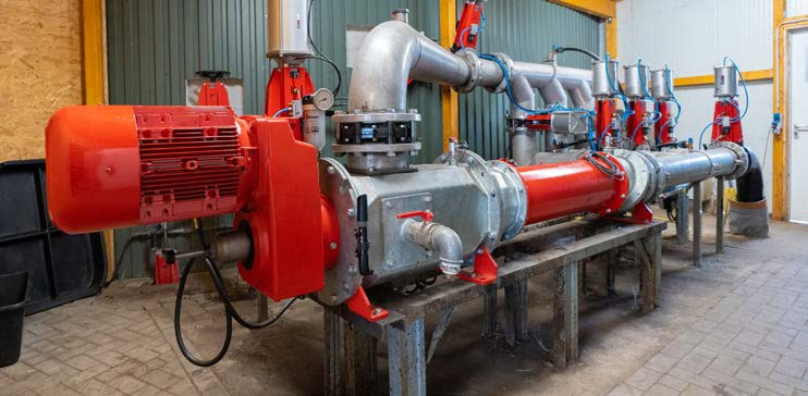Großes industrielles Pumpensystem mit roten und silbernen Komponenten, das auf einem Metalltisch in einer Werkstatt installiert ist.